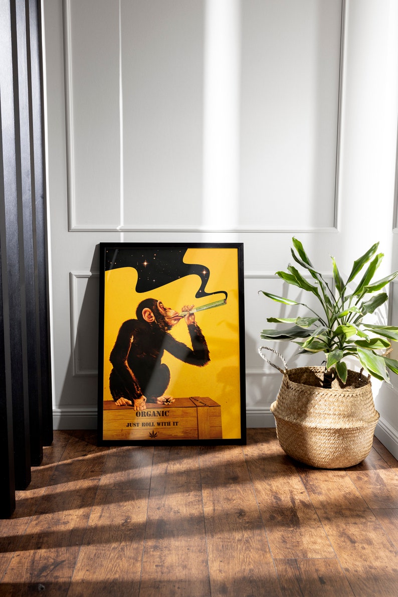 May include: A black framed poster with a yellow background featuring a cartoon chimpanzee smoking a joint. The text on the poster reads "Organic Just Roll With It".