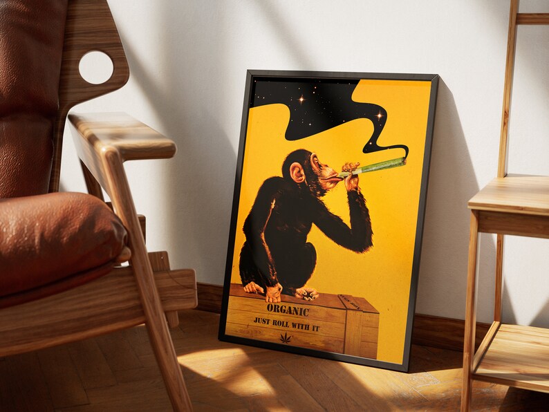May include: A framed poster with a yellow background featuring a cartoon chimpanzee smoking a joint. The chimpanzee is sitting on a wooden crate with the text "Organic Just Roll With It" and a marijuana leaf symbol.