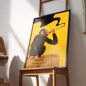 May include: A framed poster with a yellow background featuring a cartoon monkey smoking a joint. The monkey is wearing a black suit and has a black cloud of smoke above its head. The poster says "Organic Just Roll With It" and has a marijuana leaf symbol.