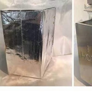 May include: A silver metal vent cover with a louvered design. The vent cover is attached to a wall and has a rectangular shape. The vent cover is labeled "HOT".