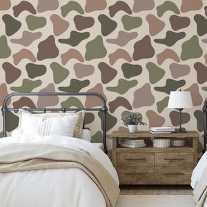 May include: Bedroom scene with two beds, a nightstand, and a patterned wall. The wall features a repeating pattern of abstract shapes in shades of brown, green, and beige. The beds have white bedding and tan blankets. A lamp sits on the nightstand.