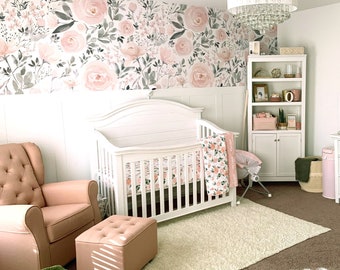 May include: A white crib with a floral patterned sheet and blanket, a pink and white ottoman, and a white armchair with a floral pattern. The room has a white ceiling fan with crystal accents, a white bookshelf with shelves filled with decorative items, and a white wall with a floral wallpaper.