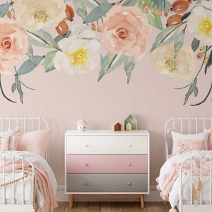 May include: Two white twin beds with pink bedding and a white dresser with three drawers. The dresser has a pink, white, and gray color scheme. The wall behind the beds is a light pink color and features a floral decal with watercolor-style flowers in shades of pink, white, and green.
