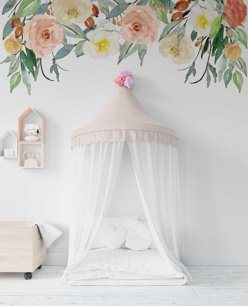 May include: A white canopy bed with a pink and white canopy and a white mattress. The bed is in a room with white walls and a floral decal on the wall.