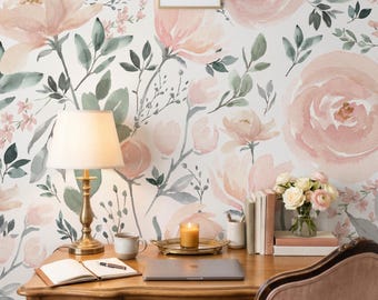 May include: A wooden desk with a brass lamp, an open notebook, a laptop, a candle on a gold tray, a cup, and a vase of flowers. The wall behind features a large-scale watercolor floral wallpaper with soft pink roses and green foliage.
