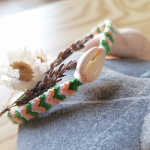 Puede incluir: Un brazalete de la amistad con rayas verdes, blancas y naranjas y un dije de concha blanca.