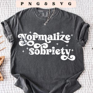 May include: Dark gray t-shirt with the words "Normalize Sobriety" in a white, stylized font. The shirt has a crew neck and short sleeves. The image also includes the text "PNG & SVG" and "Digital Download".