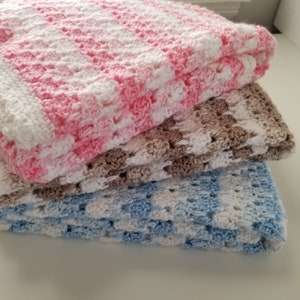May include: Three crocheted baby blankets stacked on top of each other. The top blanket is pink and white, the middle blanket is brown and white, and the bottom blanket is blue and white.