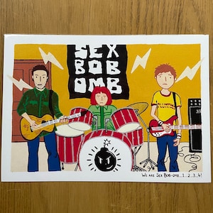 May include: A hand-drawn illustration of a band called "Sex Bob-omb" performing on stage. The band members are wearing colorful clothing and playing musical instruments. The illustration is set against a yellow background with black lightning bolts.