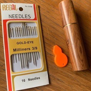 May include: A package of 16 gold-eye milliners needles, size 3/9, in a white and yellow box with the brand name "REGAL" and the number "300M". The needles are packaged with a wooden case and a small orange needle threader.