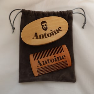 May include: A brown wooden beard brush and comb set with the name Antoine engraved on both pieces. The set is packaged in a brown velvet drawstring bag.