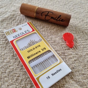 May include: A package of 16 gold-eye milliners needles, size 3/9, in a red and white box with the brand name "Regal Needles" printed on it. The box is sitting on a beige fabric surface.