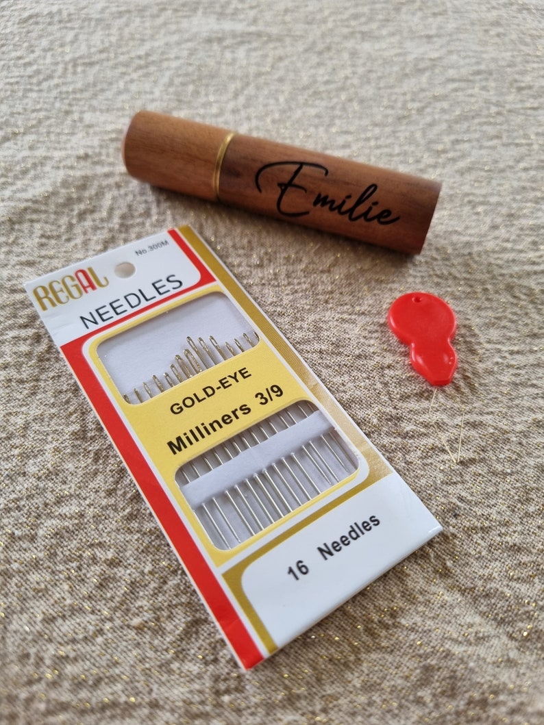 May include: A package of 16 gold-eye milliners needles, size 3/9, in a red and white box with the brand name "Regal Needles" printed on it. The box is sitting on a beige fabric surface.