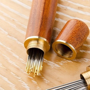May include: A wooden case with a brass top, containing a bundle of sewing needles. The case is made of dark wood with a light wood grain pattern.