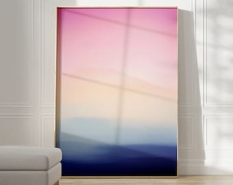May include: A framed abstract landscape painting with a gradient of pink, orange, blue, and purple colors. The painting is hanging on a white wall with a white trim.