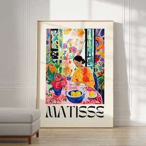 Op de afbeelding: Een kleurrijk schilderij van een vrouw die aan een tafel zit met een kom citroenen en een vaas met bloemen. Het schilderij is ingelijst en heeft de tekst "MATISSE" onderaan.