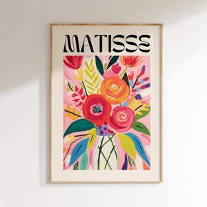 Può includere: Una stampa incorniciata con uno sfondo rosa e un bouquet di fiori colorati in un vaso bianco. Il testo "MATISSE" è in cima alla stampa.