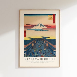 May include: A vintage woodblock print by Utagawa Hiroshige depicting a bustling street scene in Edo, Japan. The print features Mount Fuji in the distance, with a vibrant sunset sky and a detailed cityscape below. The text reads "SURUGA STREET (SURUGA-CHO) FROM THE SERIES ONE HUNDRED FAMOUS VIEWS OF EDO."
