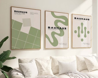 Può includere: Tre poster minimalisti con il testo "Bauhaus" in nero su sfondo bianco. I poster presentano forme geometriche astratte in verde su sfondo crema. I poster sono appesi a una parete bianca sopra un divano bianco con cuscini verdi e una coperta bianca.