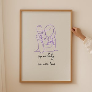 Peut inclure: Une impression encadrée avec un dessin au trait violet d'une personne tenant un verre de vin. Le texte sous le dessin dit "sip me baby one more time".
