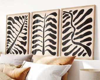 May include: Three black and white abstract art prints with a natural wood frame. The prints are hanging above a bed with a brown linen duvet cover and white pillows.