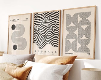 Peut inclure: Trois impressions d'art géométriques noir et blanc avec le texte "BAUHAUS" et l'année "1919" sur un mur de chambre à coucher au-dessus d'un lit avec une literie brune et blanche.