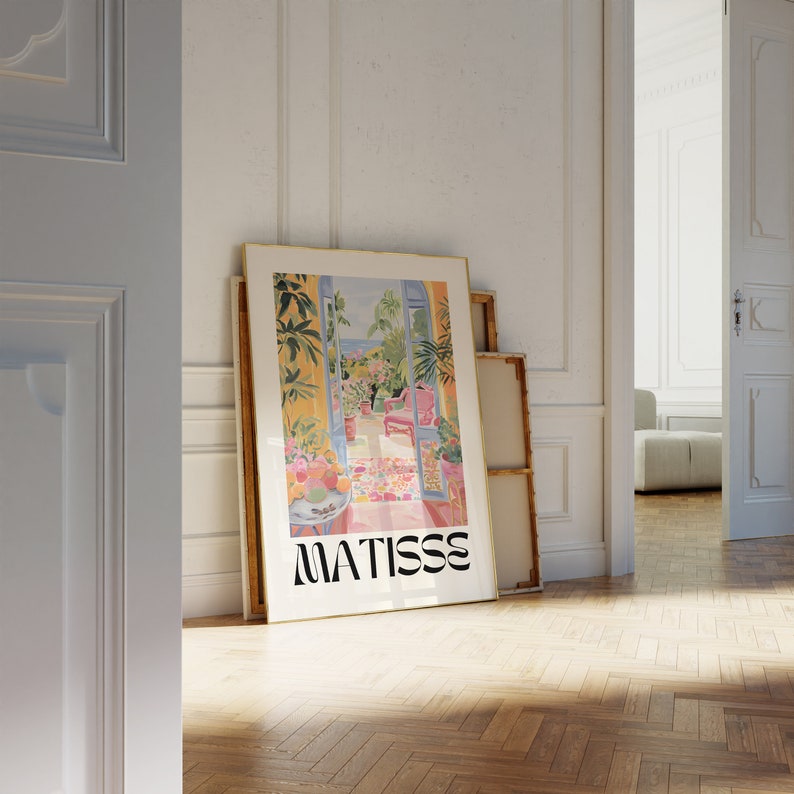 Framed Matisse-inspired poster leaning against a wall in a classic-style room with white paneled walls and wooden herringbone flooring. The vibrant artwork contrasts with the neutral space, creating a stylish, elegant atmosphere.