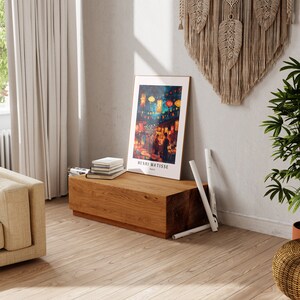 May include: A wooden bench with a framed print of a painting by Henri Matisse. The print depicts a night scene with colourful lanterns and people walking in a street. The bench is decorated with a stack of books and rolled up newspapers.
