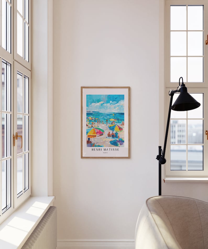 May include: A framed print of a painting by Henri Matisse depicting a beach scene with colorful umbrellas and people enjoying the sun and water. The print is in a wooden frame and has the artist's name and "Paris" printed below the image.