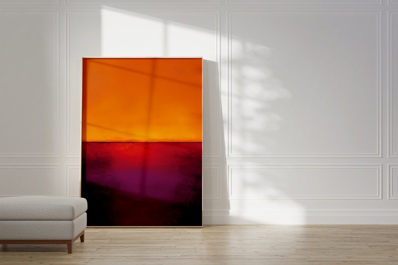 May include: Abstract art piece with a color field design. The artwork features a gradient of orange at the top, transitioning to a deep red and purple at the bottom. The painting is framed in a gold-colored frame and leans against a white wall.