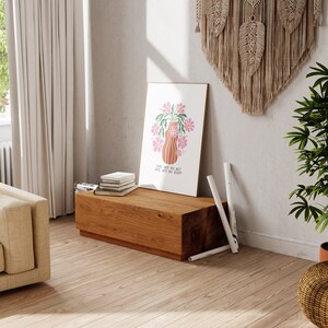 a living room with a plant and a picture on a stand