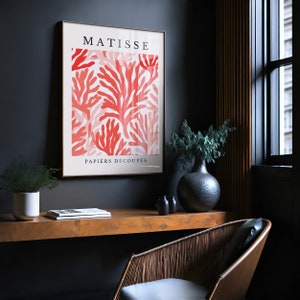 Op de afbeelding: Een ingelijste print van een Matisse-kunstwerk met een rood koraalontwerp met de tekst "MATISSE PAPIERS DECOUPES".