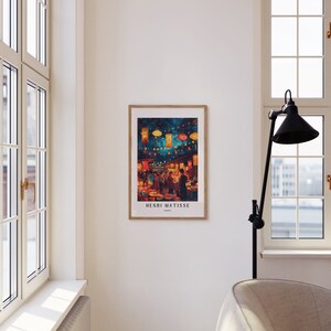 May include: A framed print of a painting by Henri Matisse depicting a bustling street scene at night with colourful lanterns and people walking by. The print is in a wooden frame and has the artist's name and "Paris" written below the image.