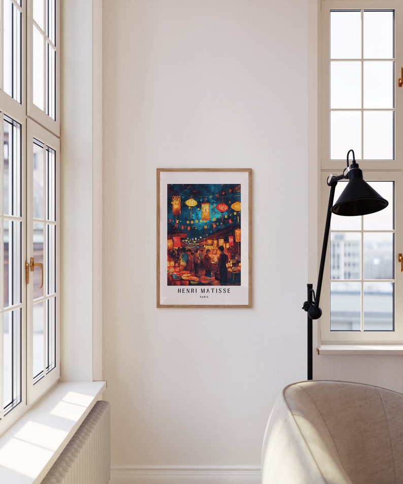 May include: A framed print of a painting by Henri Matisse depicting a bustling street scene at night with colourful lanterns and people walking by. The print is in a wooden frame and has the artist's name and "Paris" written below the image.