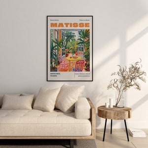 May include: A colorful poster with the text "MATISSE" in orange letters. The poster features a painting of a patio with a table and chairs, surrounded by lush greenery. The text "06200 NICE, FRANCE" is at the bottom left corner of the poster.