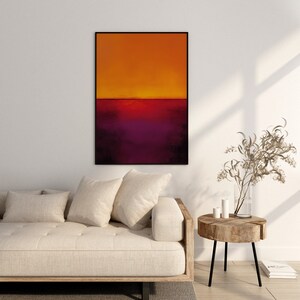 May include: Abstract art print in a black frame. The artwork features a gradient of colors, with orange at the top transitioning to deep purple at the bottom. The painting is displayed above a beige sofa and a wooden side table.