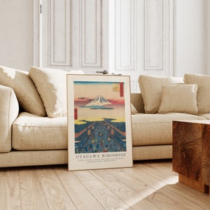 May include: A vintage Japanese woodblock print by Utagawa Hiroshige depicting a view of Mount Fuji from a street in Edo, now Tokyo. The print is framed in a simple wooden frame and has a light brown background.