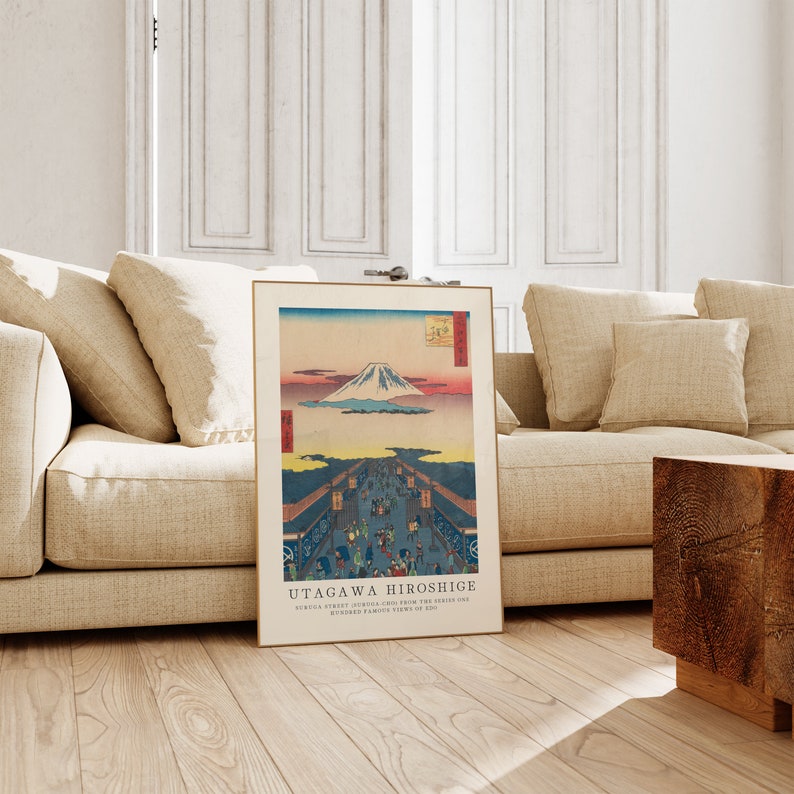 May include: A vintage Japanese woodblock print by Utagawa Hiroshige depicting a view of Mount Fuji from a street in Edo, now Tokyo. The print is framed in a simple wooden frame and has a light brown background.