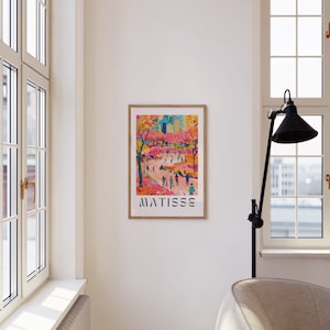 May include: A framed art print depicting a lively street scene with figures and trees. The artwork uses a bright palette of pink, orange, and blue. The word "MATISSE" is printed in a bold, sans-serif font at the bottom of the print.