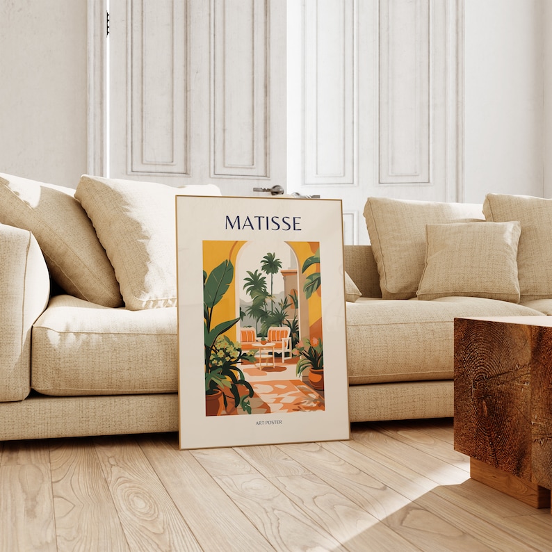 May include: A poster with a colorful illustration of a tropical garden with a yellow archway, two chairs, and palm trees. The poster is framed in gold and has the text "MATISSE ART POSTER" at the bottom.