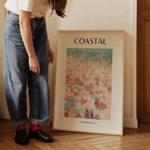 K&ouml;nnte beinhalten: Ein gerahmter Kunstdruck mit dem Titel "COASTAL", der eine Strandszene mit Menschen, bunten Sonnenschirmen und einem hellblauen Ozean zeigt. Der Druck befindet sich in einem hellen Holzrahmen und tr&auml;gt die Aufschrift "ART POSTER NO. 23".