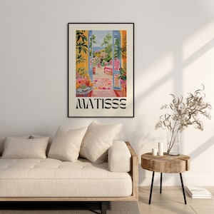 Framed Matisse-inspired poster hanging above a beige sofa in a modern living room. The space features neutral tones, a wooden side table, and minimalist decor, with sunlight casting soft shadows on the wall, creating a warm, cozy atmosphere.