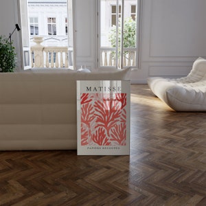 Op de afbeelding: Een ingelijste print van een Matisse-kunstwerk met een rood koraalontwerp met de tekst "MATISSE PAPIERS DECOUPES".