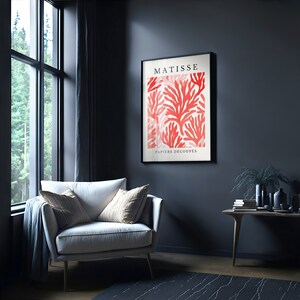 Op de afbeelding: Een ingelijste print van een rood koraalontwerp met de tekst "MATISSE PAPIERS DECOUPES" in zwart.