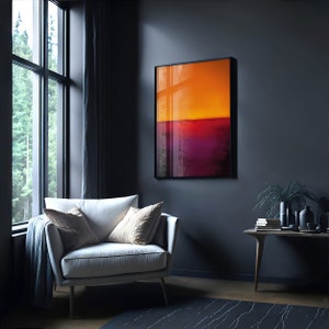 May include: An abstract art print in a black frame, featuring a gradient of orange, red, and purple hues. The artwork hangs on a dark gray wall above a white armchair with decorative pillows. A wooden side table with decor sits nearby.