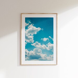 Könnte beinhalten: Ein gerahmtes Foto eines blauen Himmels mit weißen, flauschigen Wolken. Die Wolken sind über den Himmel verteilt und erzeugen so ein Gefühl von Tiefe und Bewegung.