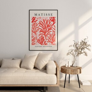 Op de afbeelding: Een ingelijste print van een rood en roze koraalontwerp met de tekst "MATISSE PAPIERS DECOUP&Eacute;S" in zwart.
