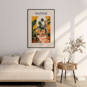 May include: A black framed art print with the text "MATISSE" in yellow letters. The print features a colorful illustration of a patio with a view of palm trees and a tiled floor. The text "ART POSTER" is at the bottom of the print.