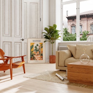 May include: A living room interior with a brown leather armchair, a beige sofa, a wooden coffee table, a potted ficus plant, and a poster with the text "MATISSE" on the wall.