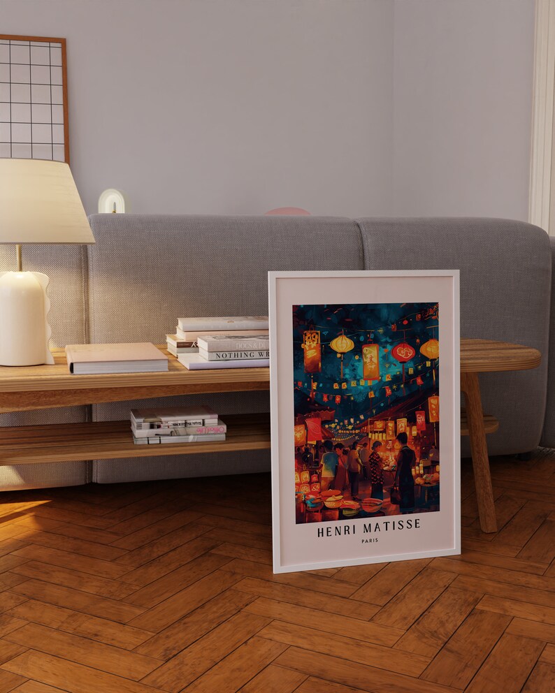 May include: A framed print of a painting by Henri Matisse depicting a street scene in Paris at night. The painting features a vibrant colour palette with red, orange, yellow, and blue hues. The street is lined with buildings and shops, and there are people walking and shopping. The painting is titled "Henri Matisse, Paris".